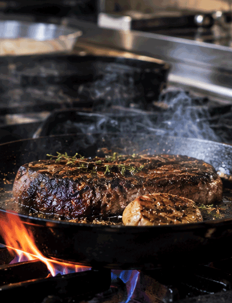 Chef's hands searing a steak in a hot skillet